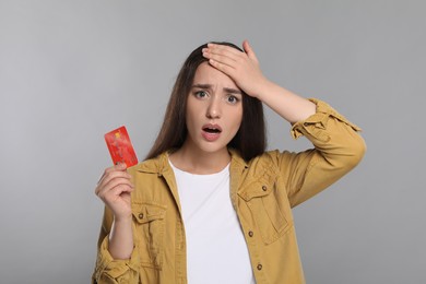 Photo of Shocked woman with credit card on light gray background. Debt problem