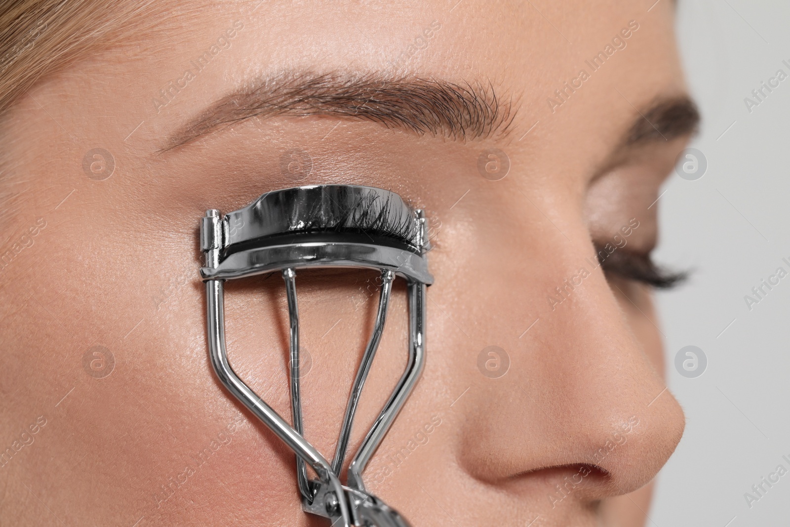 Photo of Young woman using eyelash curler on white background, closeup