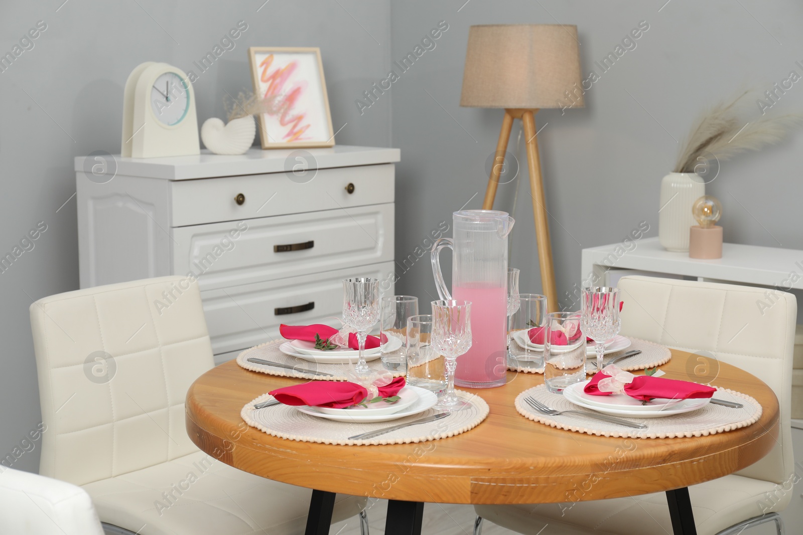 Photo of Color accent table setting. Glasses, plates, jug of beverage and pink napkins in dining room