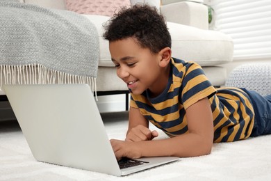 Cute African-American boy using laptop on floor at home