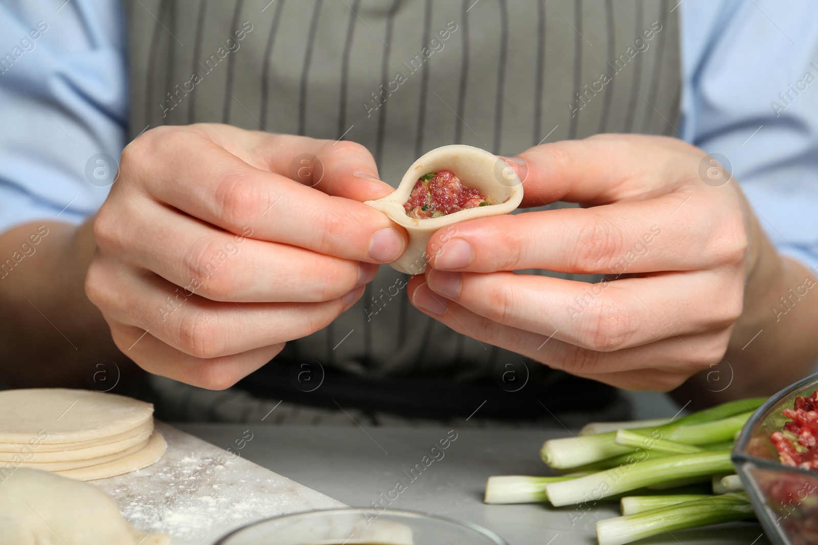 Photo of Woman making gyoza at light grey table, closeup