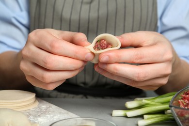 Woman making gyoza at light grey table, closeup