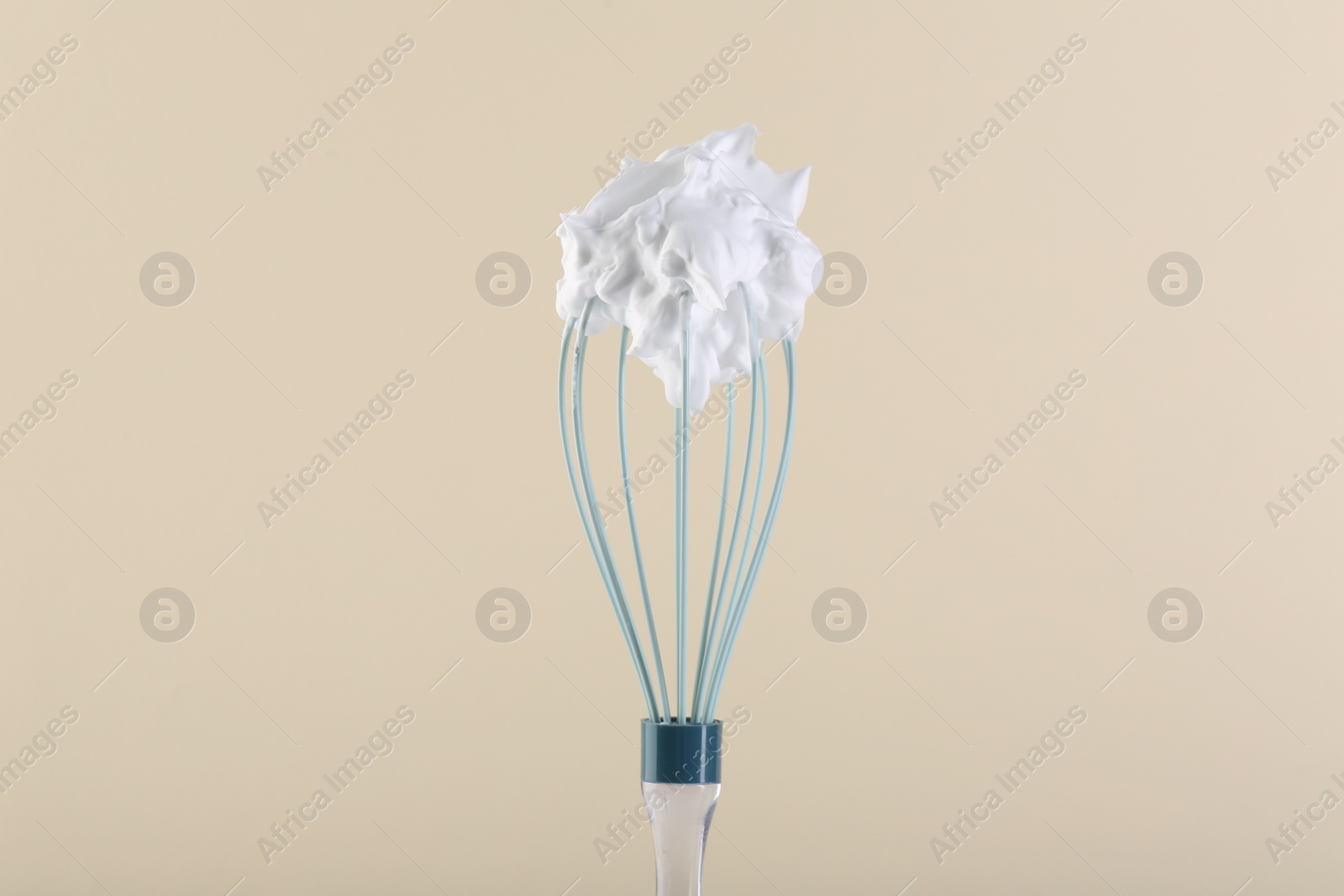 Photo of Whisk with whipped cream on beige background