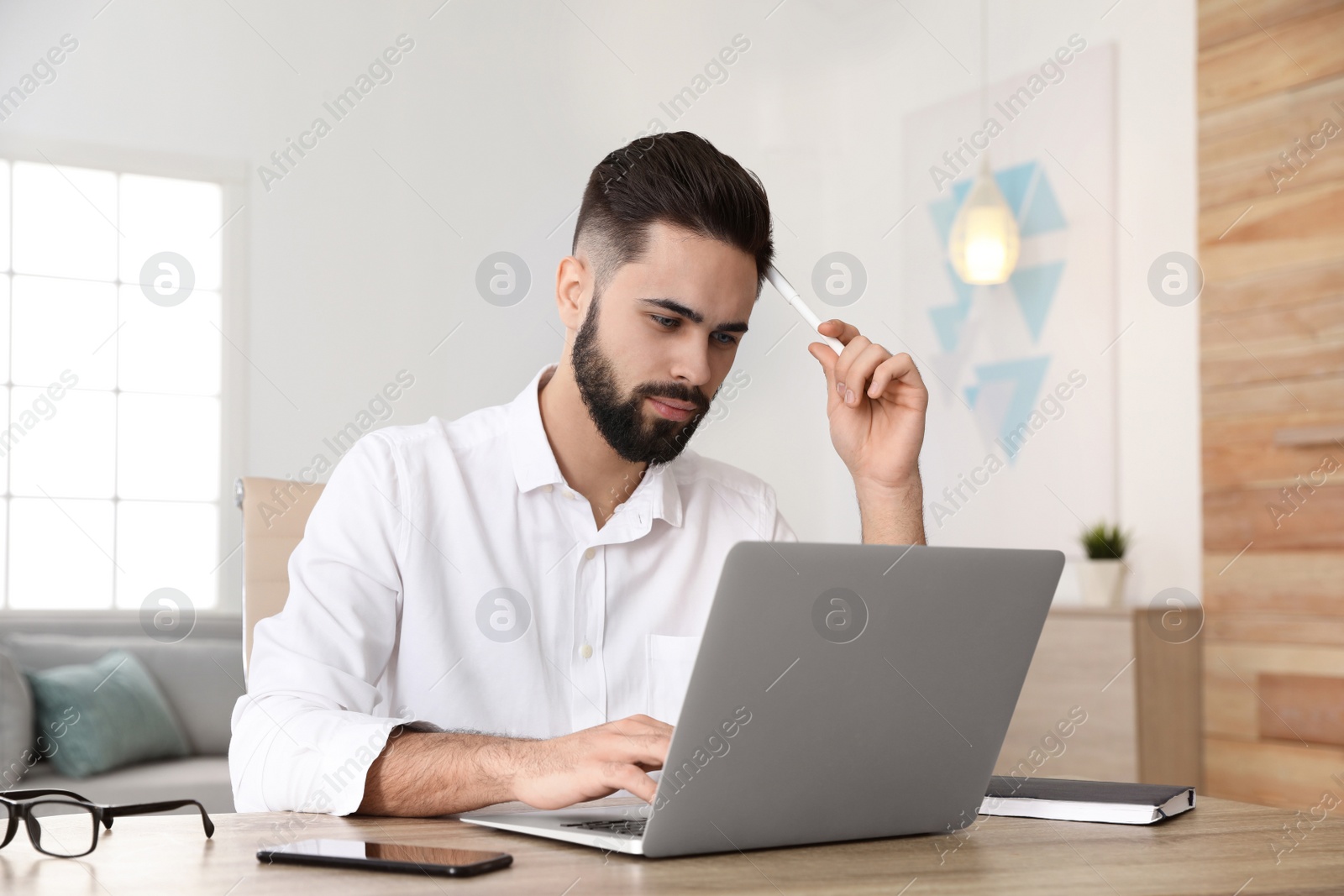 Photo of Handsome young man working with laptop at table in home office