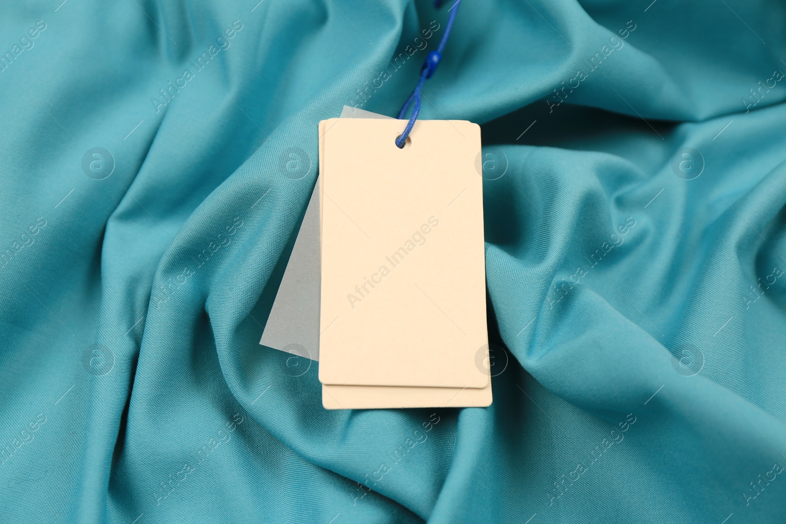 Photo of Blank white tags on light blue fabric. Space for text