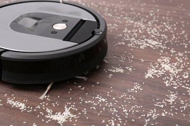 Photo of Removing groats from wooden floor with robotic vacuum cleaner at home, closeup