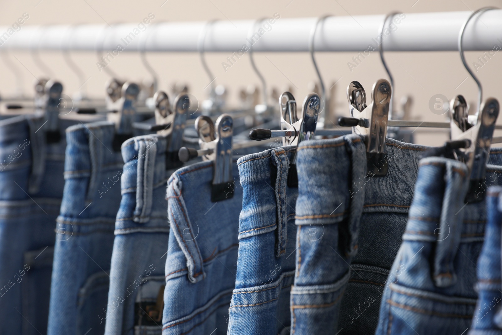 Photo of Rack with stylish jeans on beige background, closeup