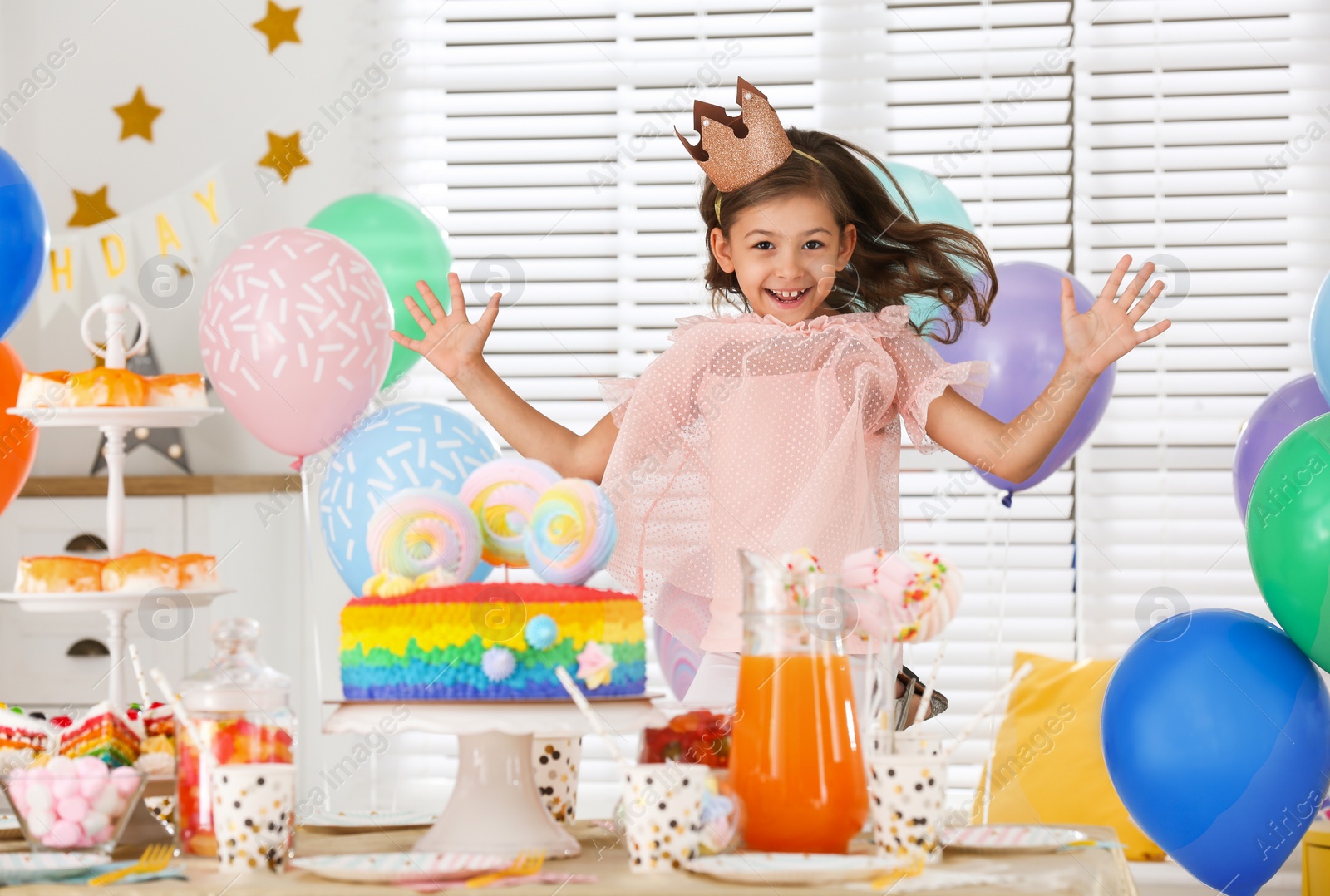 Photo of Happy girl at table with treats in room decorated for birthday party