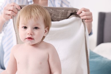 Mother wrapping her cute little baby with towel after bathing on bed