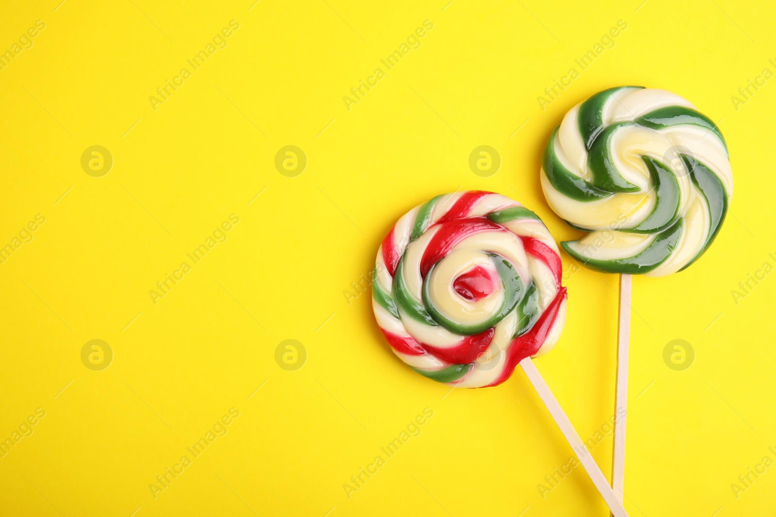 Photo of Colorful lollipops on yellow background, flat lay. Space for text