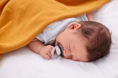 Photo of Cute newborn baby with pacifier sleeping under orange blanket on bed