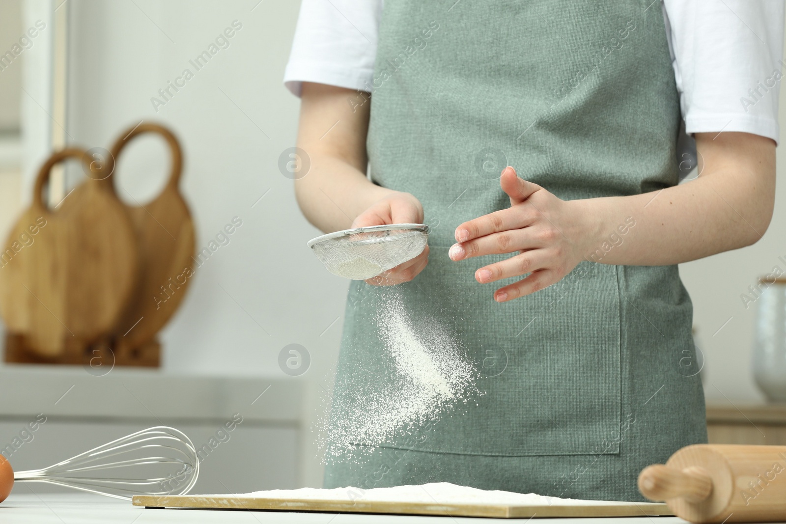Photo of Woman sieving flour at table in kitchen, closeup. Space for text