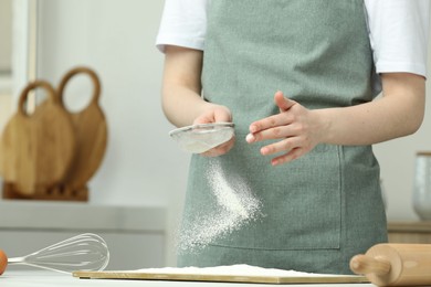 Woman sieving flour at table in kitchen, closeup. Space for text