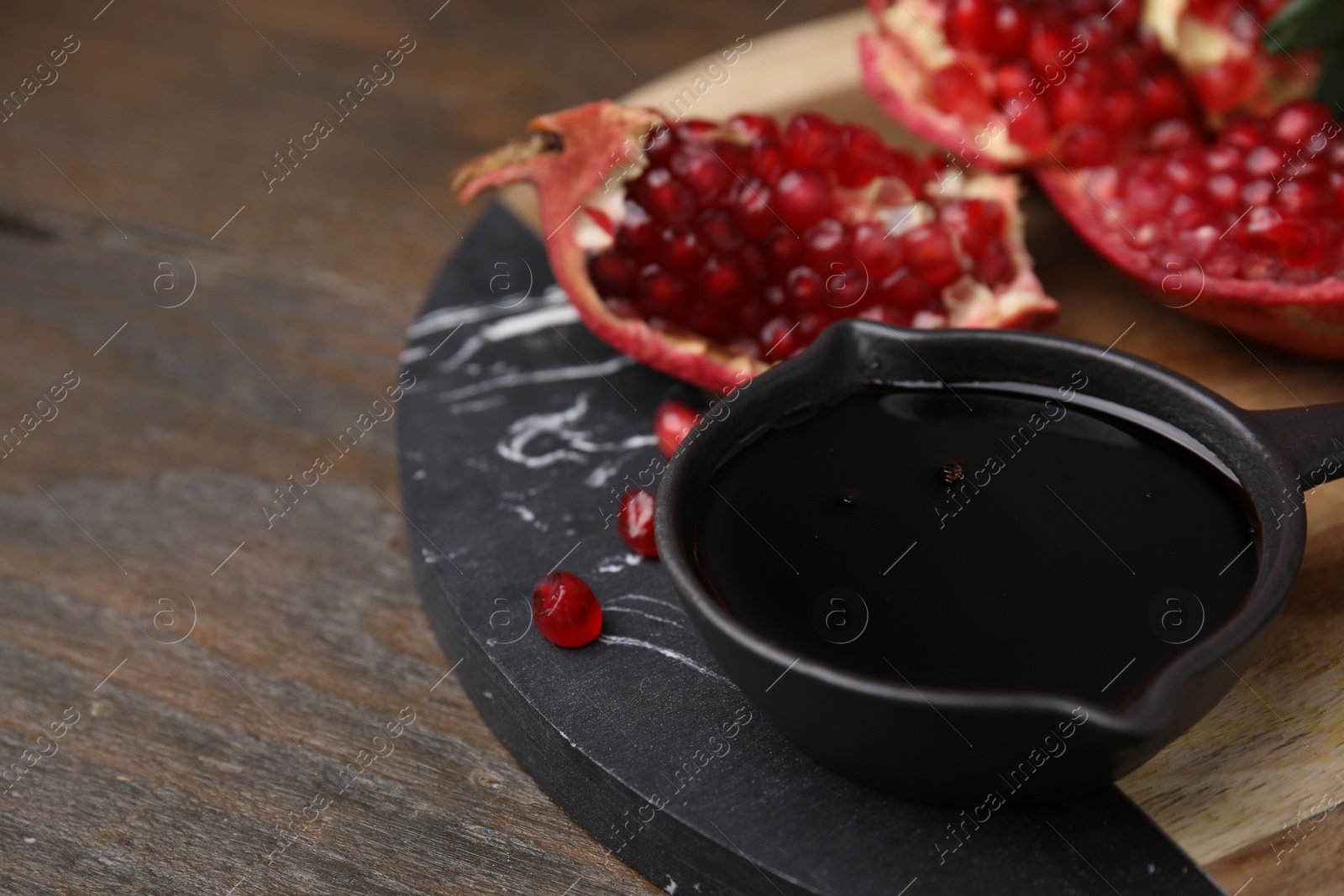 Photo of Tasty pomegranate sauce in bowl and fruit on wooden table, closeup. Space for text