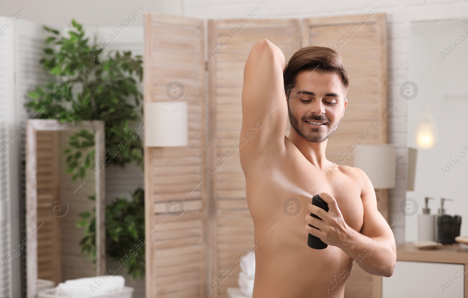 Photo of Handsome young man applying deodorant in bathroom. Space for text