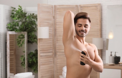 Handsome young man applying deodorant in bathroom. Space for text