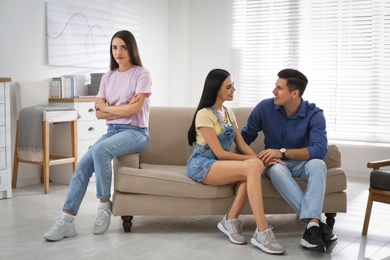 Unhappy woman feeling jealous while couple spending time together on sofa at home