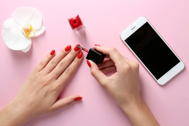 Woman applying bright nail polish on color background, top view