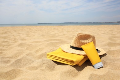 Photo of Sunscreen, towel and straw hat on sandy beach, space for text. Sun protection
