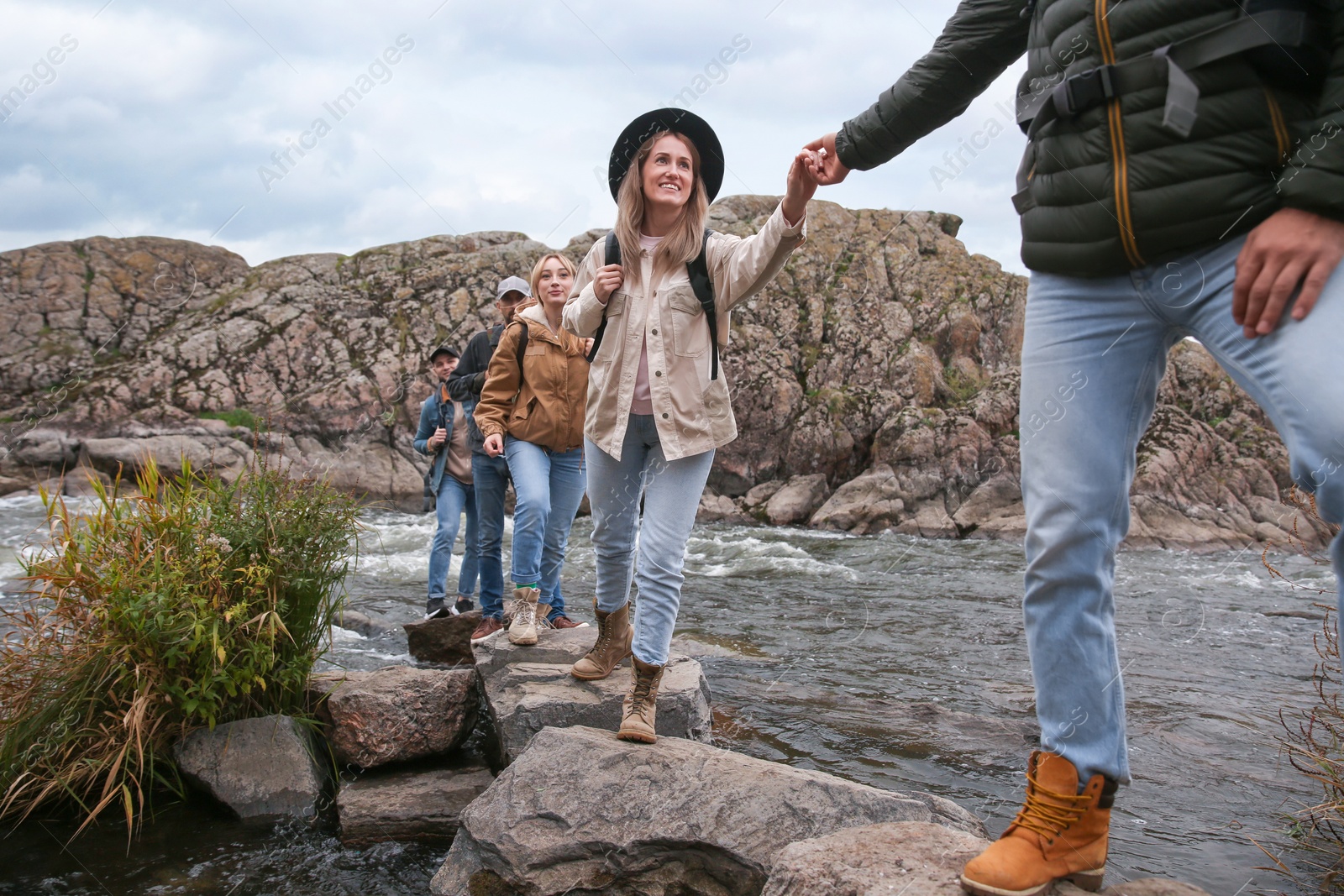 Photo of Group of friends with backpacks crossing mountain river on autumn day