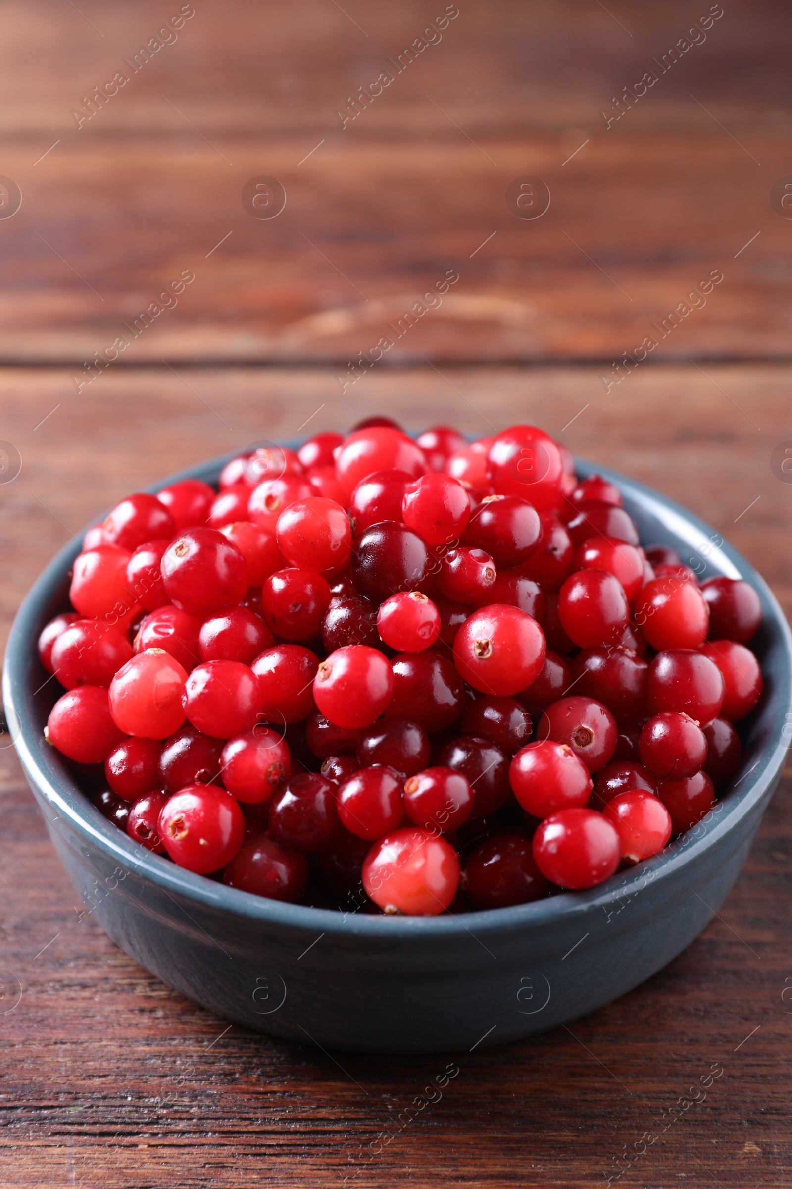 Photo of Fresh ripe cranberries in bowl on wooden table, closeup