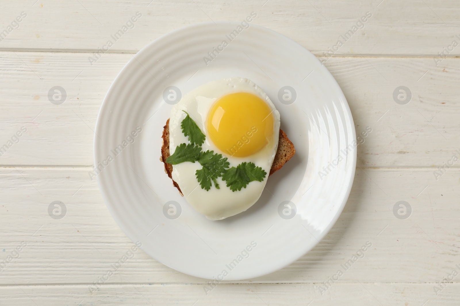 Photo of Plate with tasty fried egg and slice of bread on white wooden table, top view