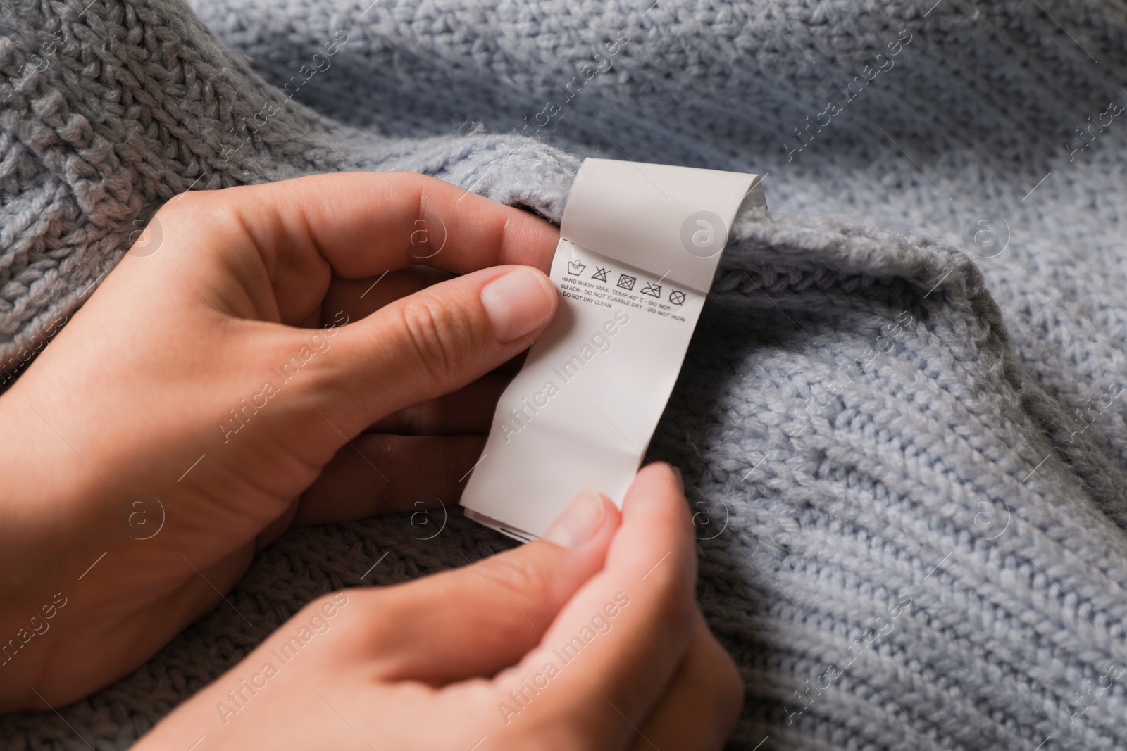 Photo of Woman holding clothing label on light blue garment, closeup