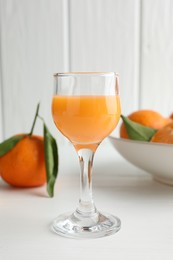 Photo of Tasty tangerine liqueur in glass and fresh fruits on white table