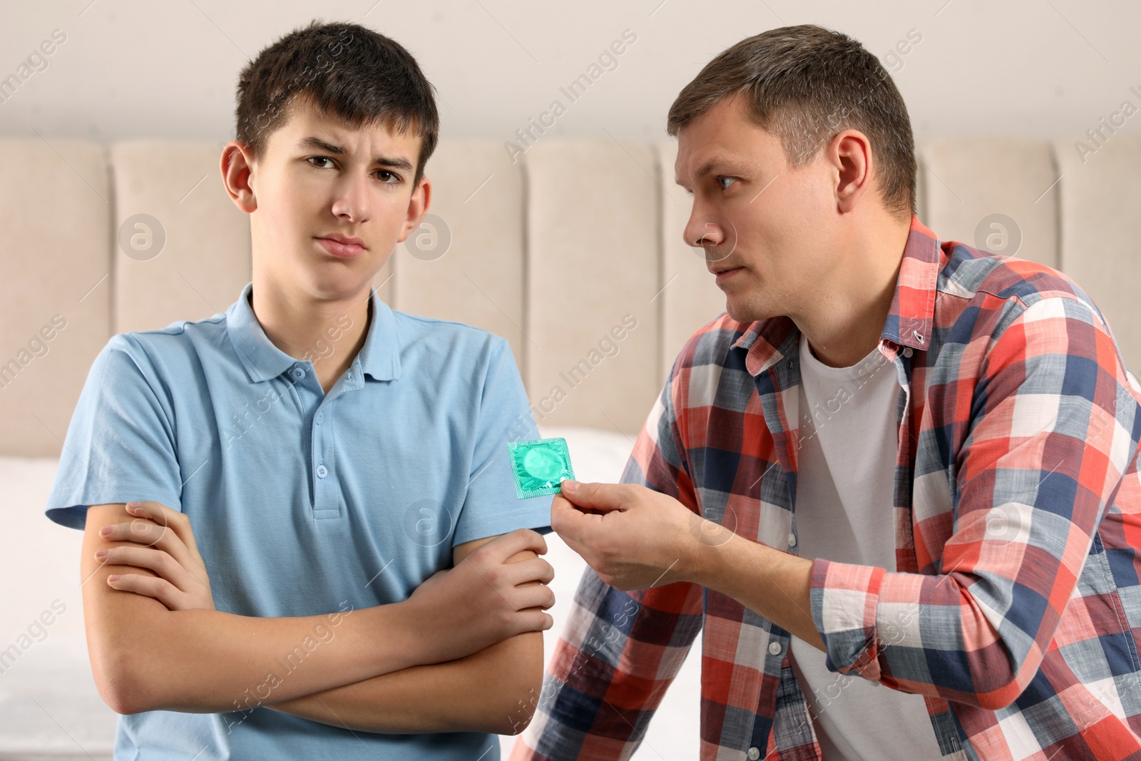 Photo of Father giving condom to his teenage son in bedroom. Sex education concept