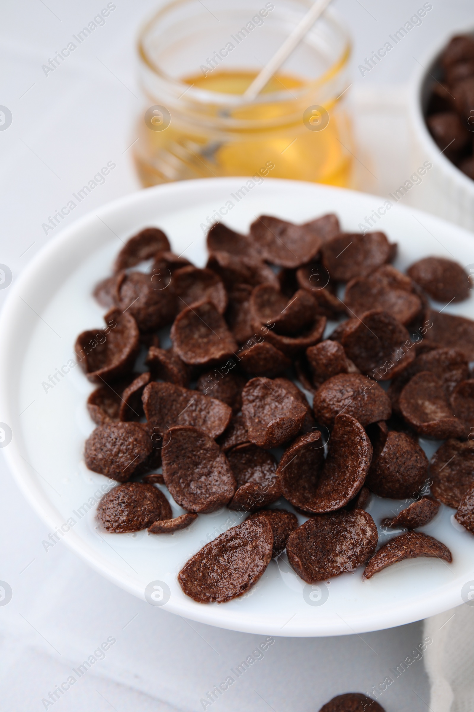 Photo of Breakfast cereal. Chocolate corn flakes and milk in bowl on white tiled table, closeup