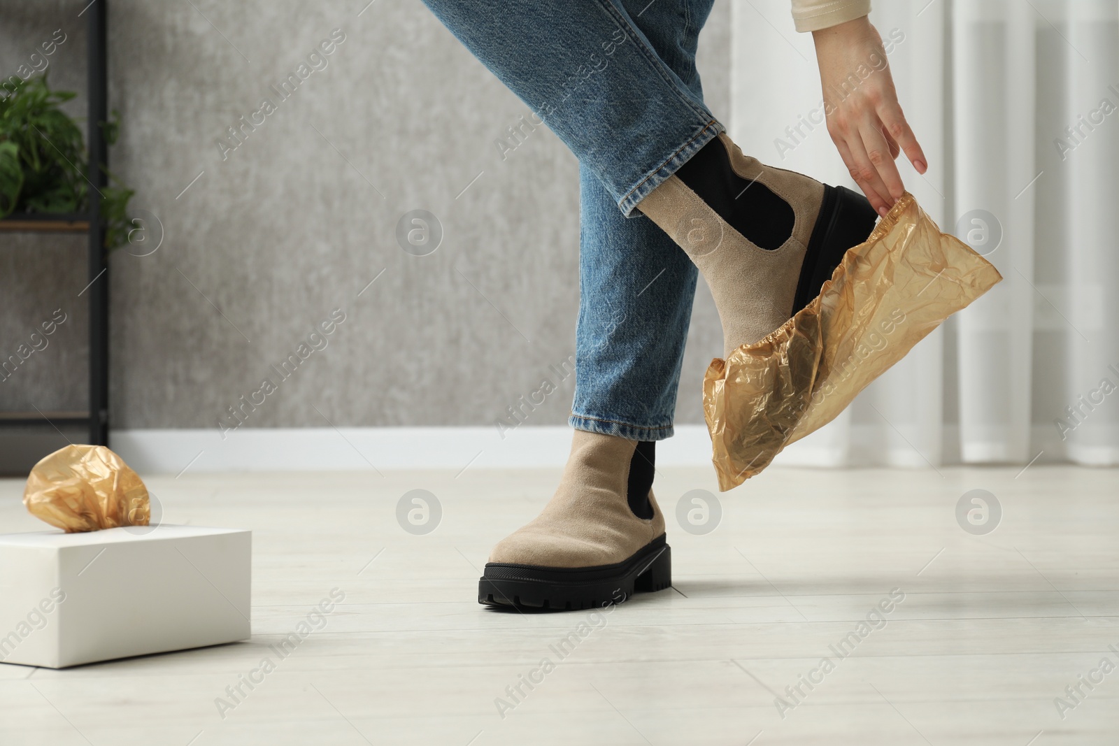Photo of Woman wearing shoe cover onto her boot indoors, closeup