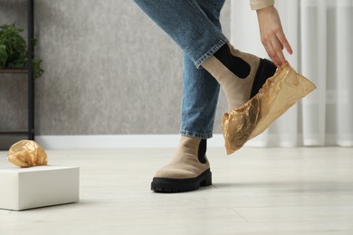 Woman wearing shoe cover onto her boot indoors, closeup