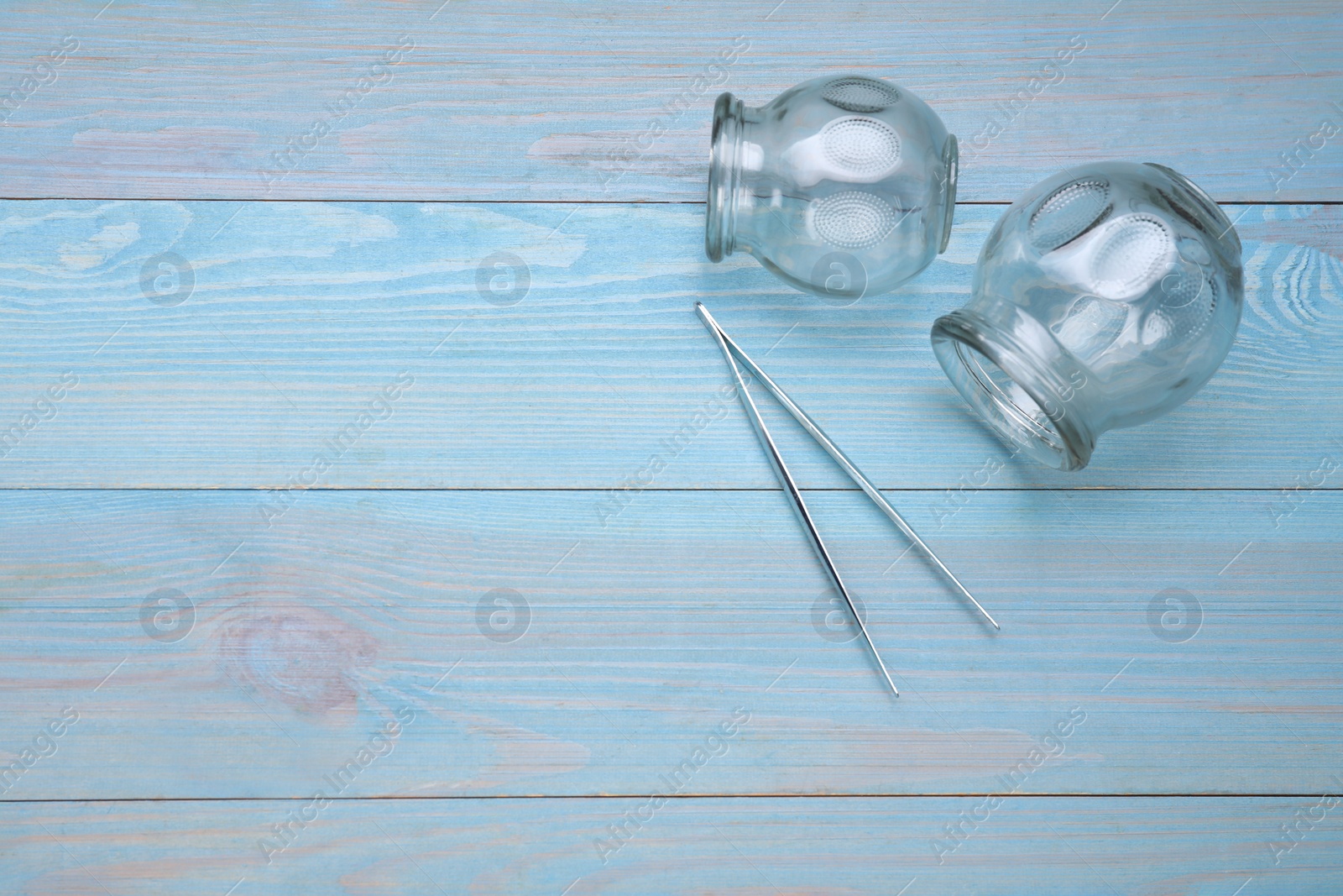 Photo of Glass cups and tweezers on light blue wooden table, flat lay with space for text. Cupping therapy