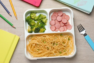 Section plate with tasty pasta, broccoli and sausage on wooden table, flat lay