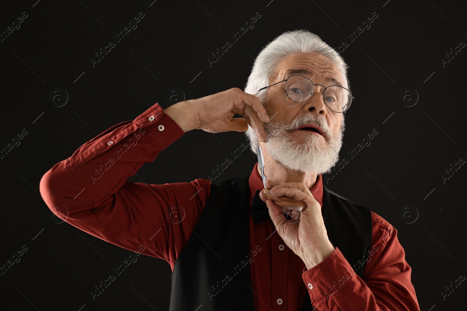 Photo of Senior man shaving beard with blade on black background