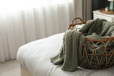 Photo of Knitted green plaid in wicker basket on bed indoors space for text.