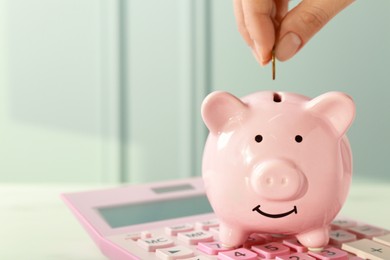 Photo of Woman putting coin into piggy bank at white table, closeup. Space for text