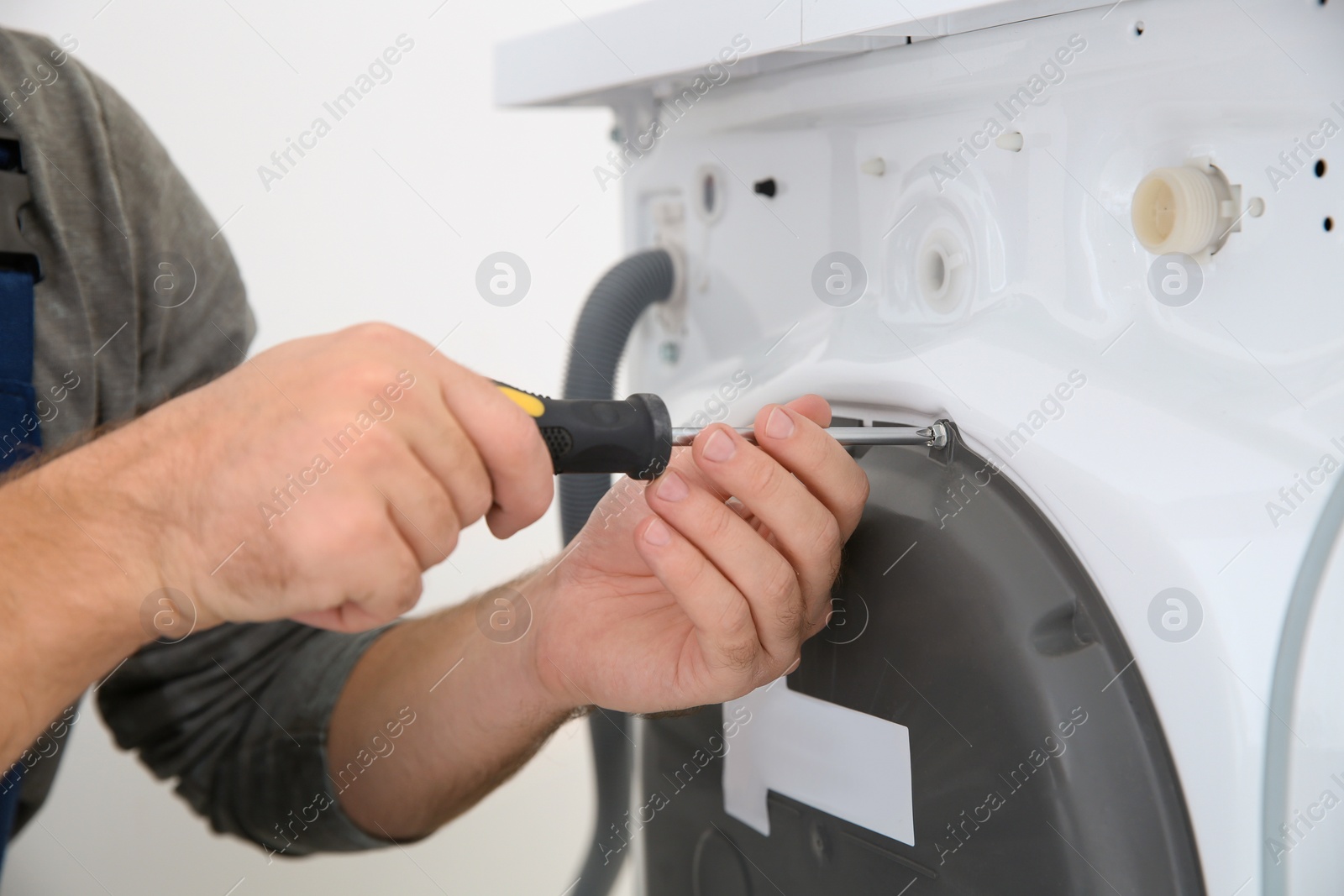 Photo of Young plumber fixing washing machine in bathroom, closeup