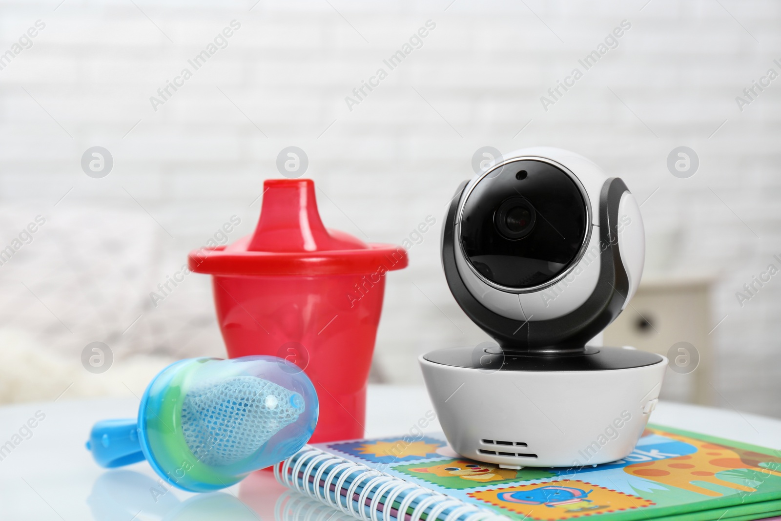 Photo of Modern CCTV security camera, baby cup, nibbler and book on table indoors