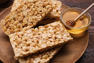 Photo of Delicious peanut bars (kozinaki) and honey on wooden table, closeup