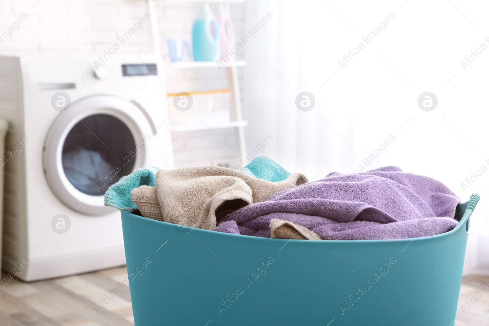 Photo of Plastic basket with dirty towels on table in laundry room