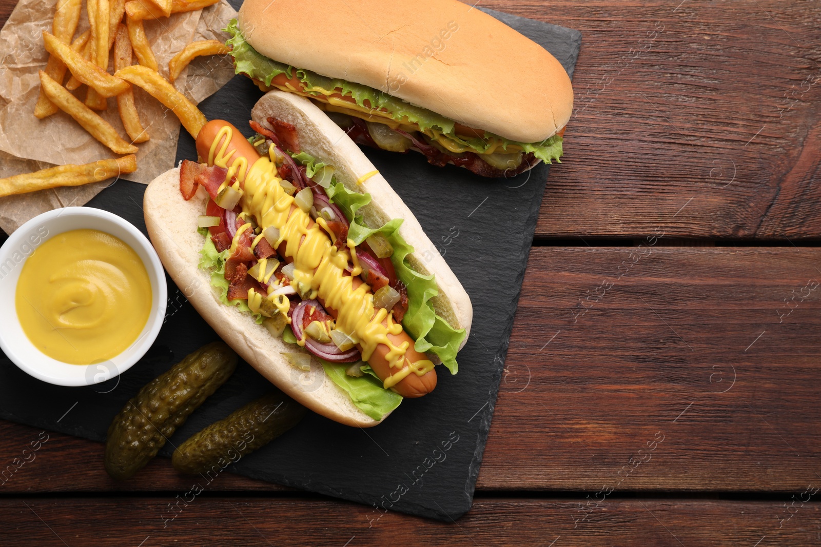 Photo of Delicious hot dogs with lettuce, onion and pickle served on wooden table, flat lay. Space for text