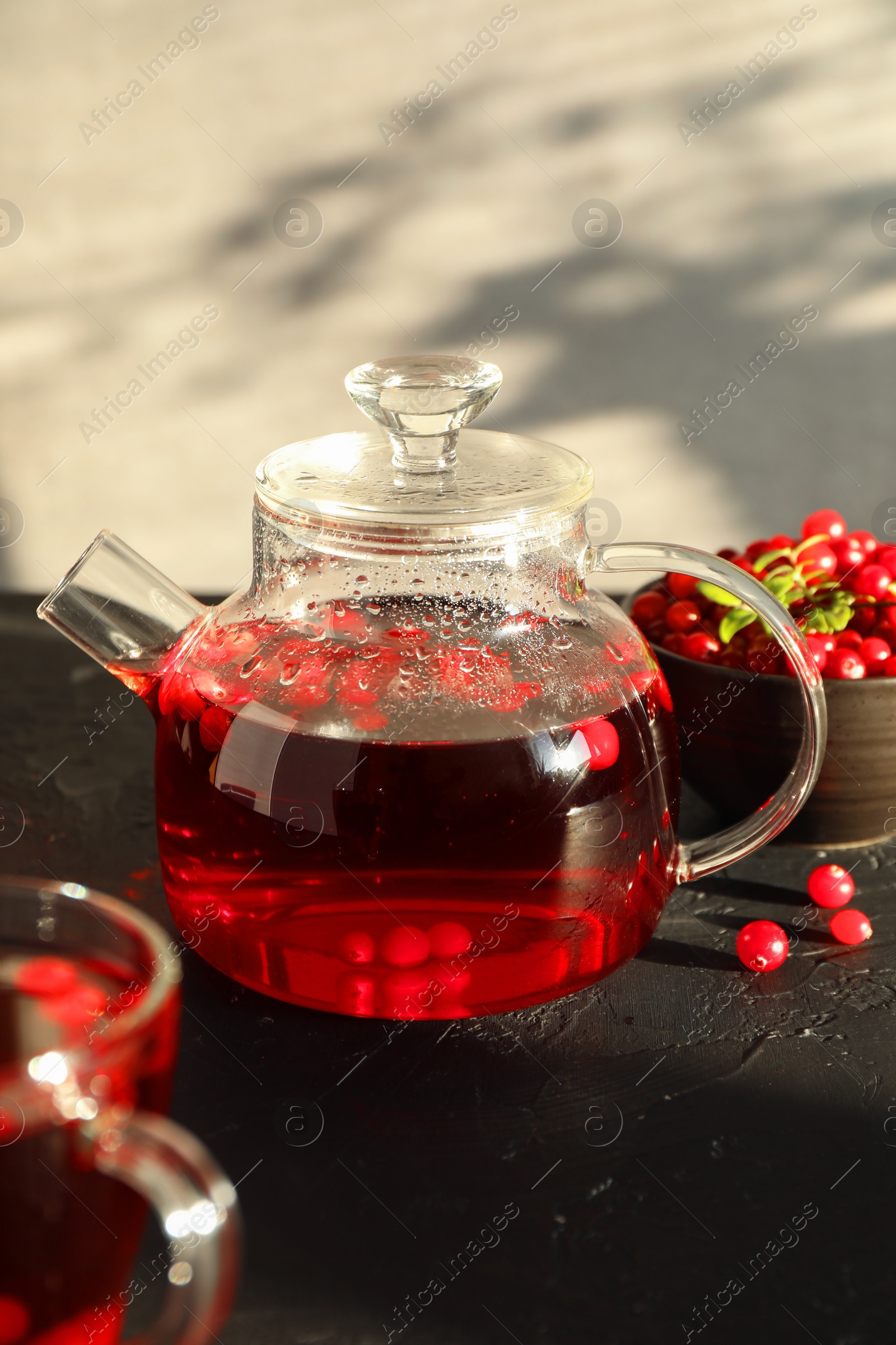 Photo of Tasty hot cranberry tea in teapot and fresh berries on black textured table