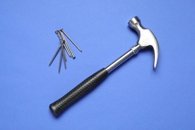 Hammer and metal nails on blue background, top view