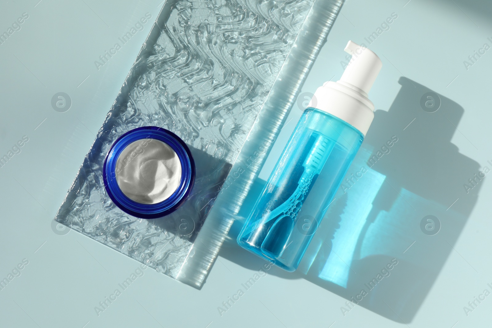 Photo of Bottle and jar of cosmetic products on light blue background, flat lay