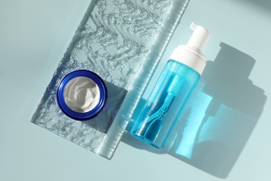 Bottle and jar of cosmetic products on light blue background, flat lay