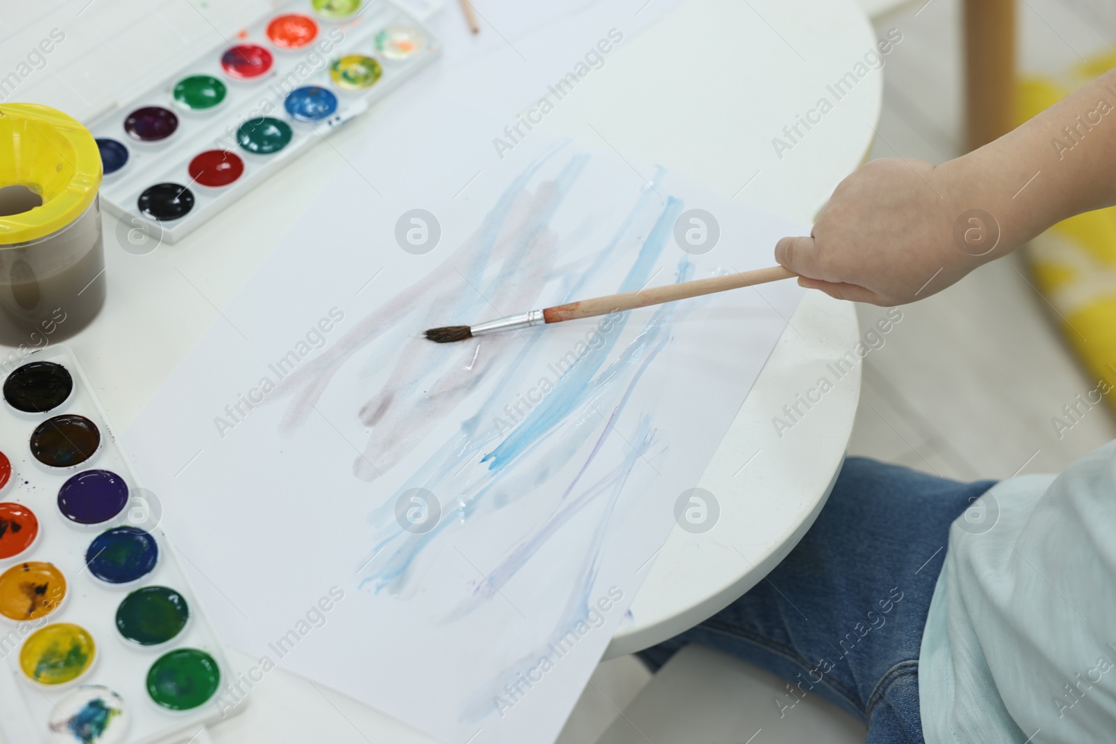 Photo of Little girl painting with brush and watercolor at white table, closeup