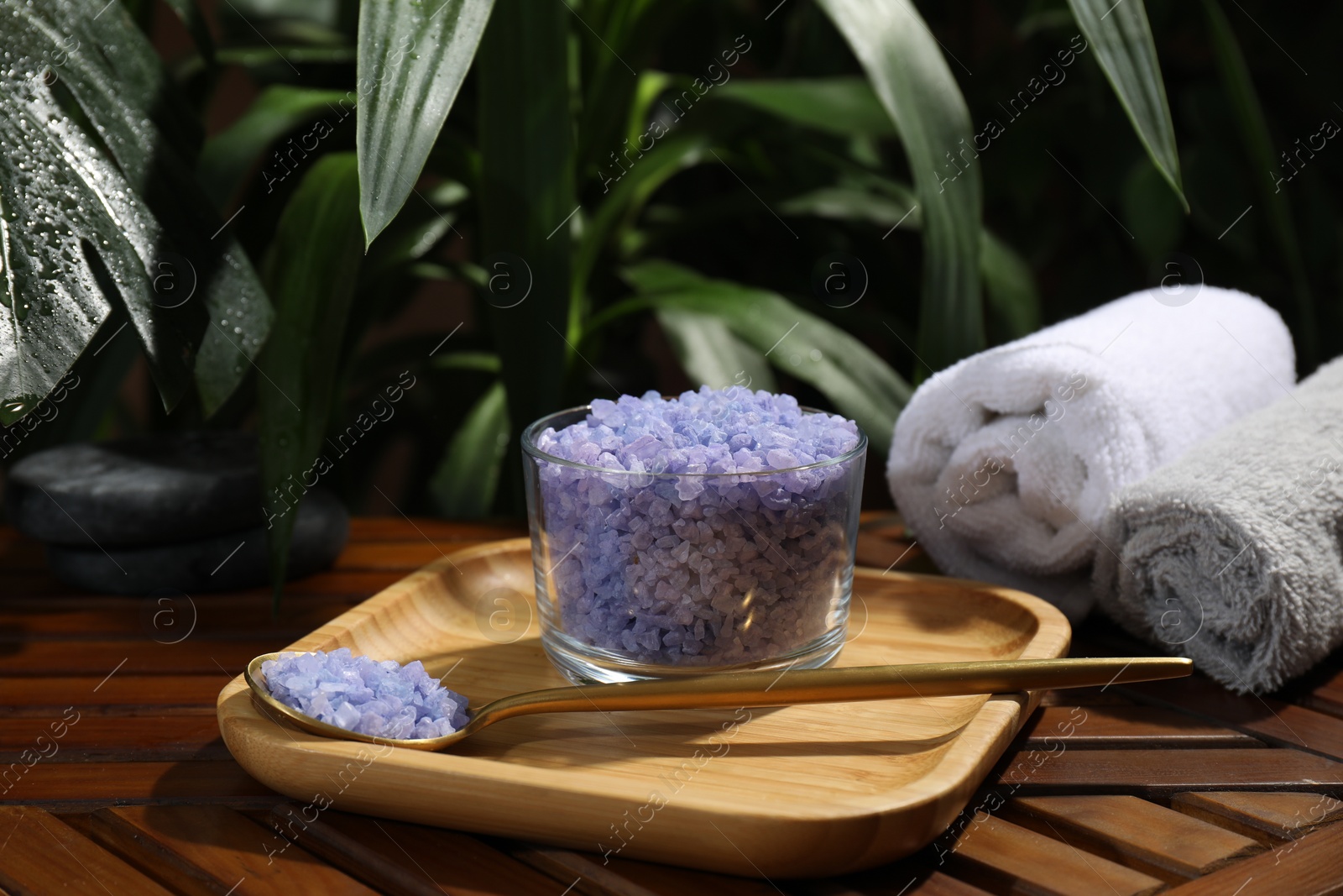 Photo of Bowl of purple sea salt, spoon and rolled towels on wooden table