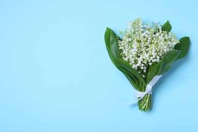 Photo of Beautiful lily of the valley flowers on light blue background, top view. Space for text