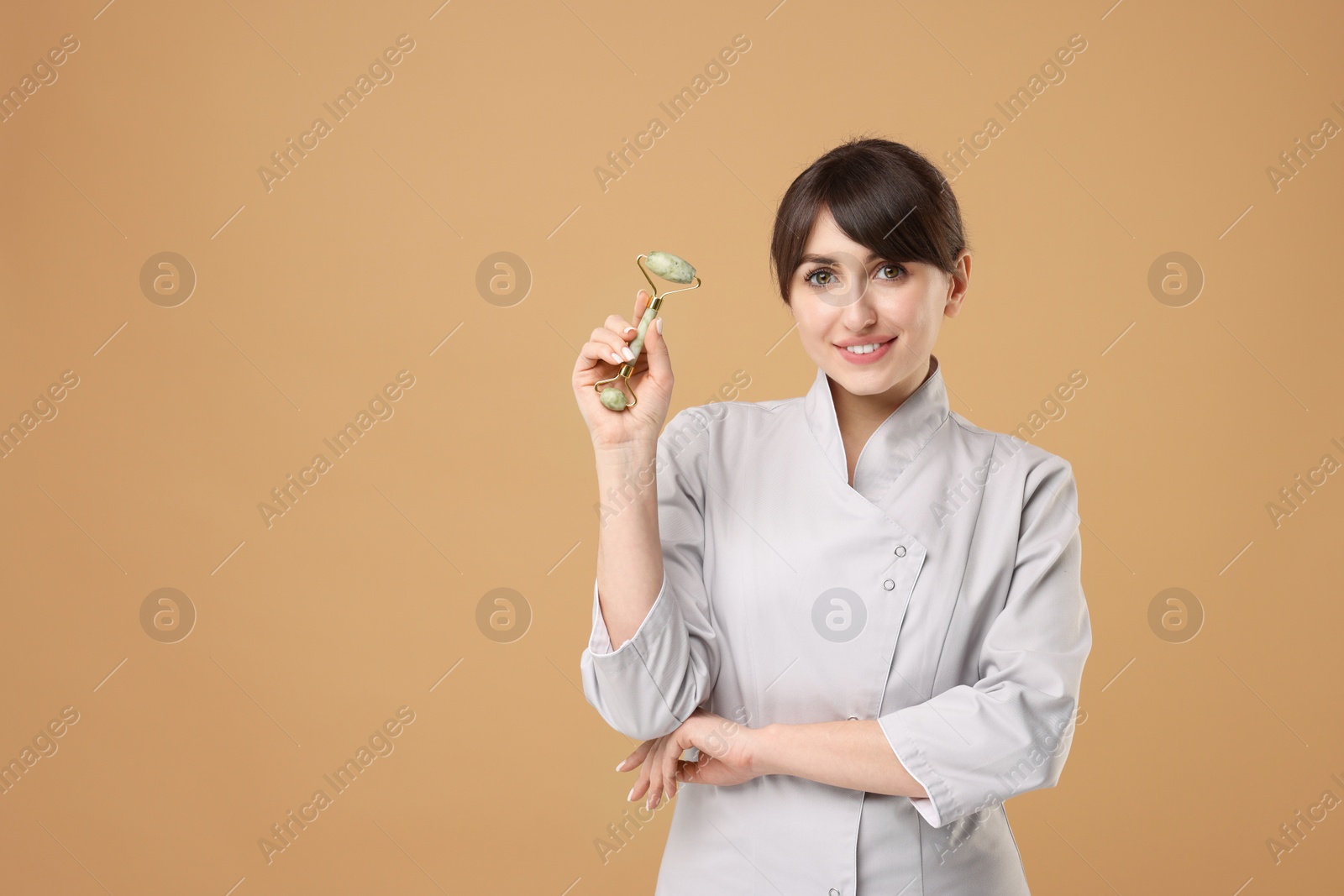 Photo of Cosmetologist with facial roller on beige background, space for text